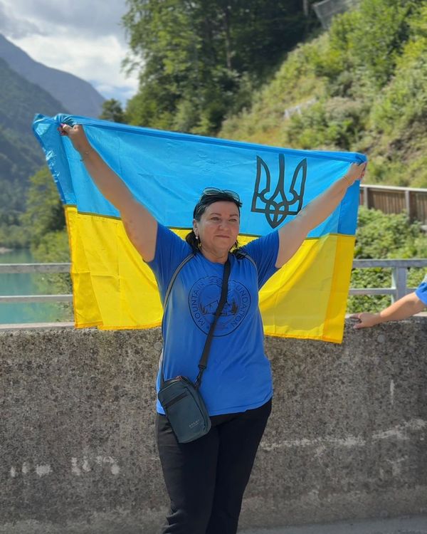 Учасниця заходу Mountain Seed Foundation у синій футболці з друком тримає прапор України